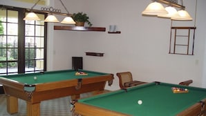 Zwei Billardtische mit grüner Spielbahn, Holzrahmen und ein Stuhl in einem Raum mit Schachbrettmuster.