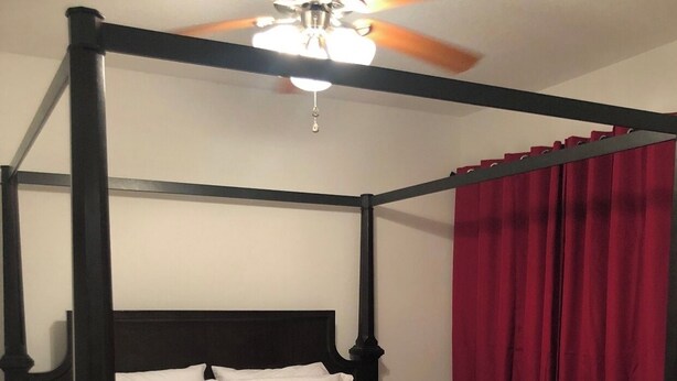 Ein Himmelbett mit weißen Leinentüchern, einem Deckenventilator und roten Vorhängen.