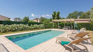 Una piscina rectangular amb una terrassa de fusta i gandules.