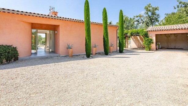 Una casa moderna amb un camí de grava, un porxo cobert i alts cipressos.