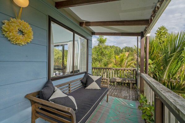 A covered outdoor seating area with a bench and a table, overlooking a lush garden.