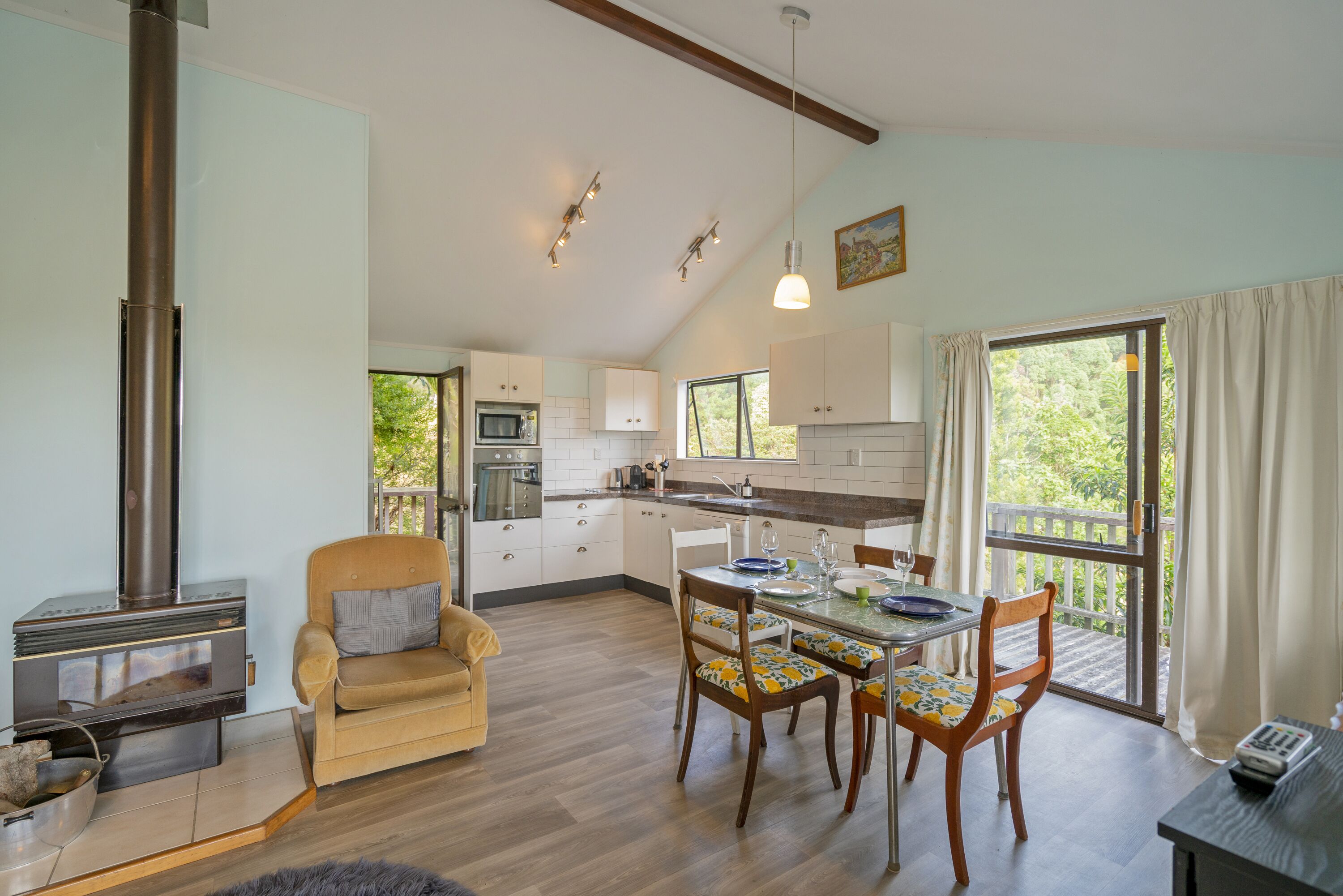 Une cuisine moderne avec des meubles blancs, un coin repas avec des chaises en bois, un canapé et une grande fenêtre avec des rideaux.