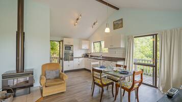Une cuisine moderne avec des meubles blancs, un coin repas avec des chaises en bois, un canapé et une grande fenêtre avec des rideaux.