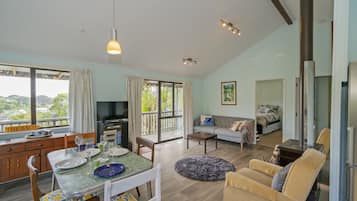 A spacious living area with a dining table, sofa, and a view of greenery outside.