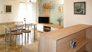 Ein modernes Wohnzimmer mit Sofa, Fernseher, Esstisch, Stühlen und einer Küchenzeile.