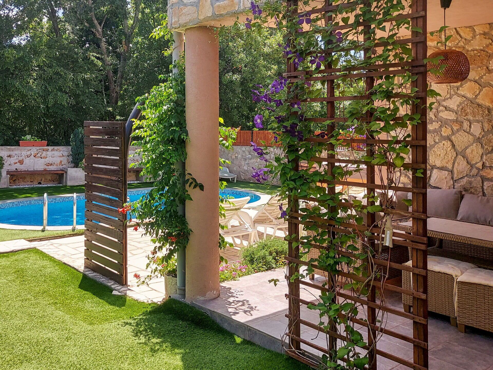 A backyard with a swimming pool, a wooden pergola, and a wicker sofa.