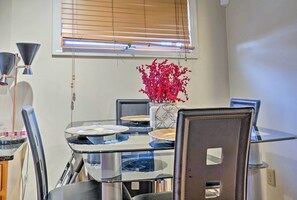 Un comedor con una mesa de vidrio, sillas y un florero con flores rojas.