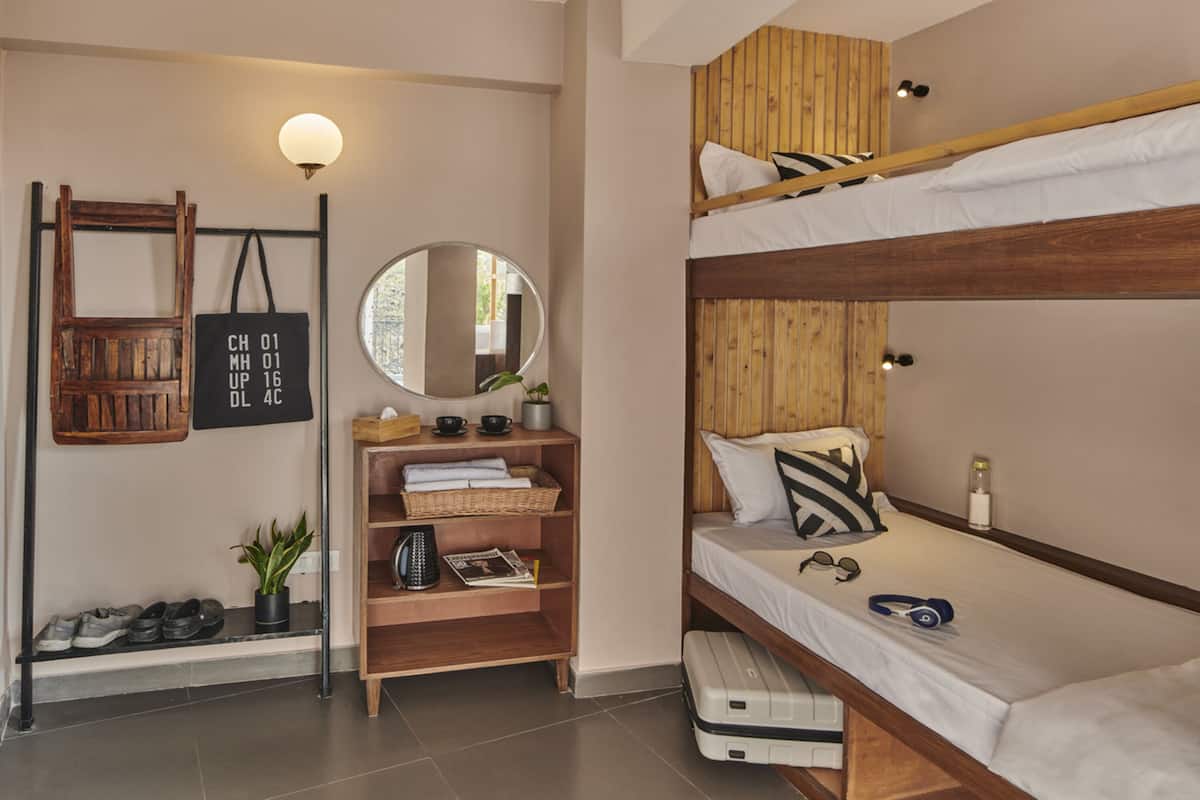 Une petite pièce comprenant deux lits superposés, un petit bureau avec un miroir, des étagères avec des livres et une plante, et un luminaire fixé au mur.