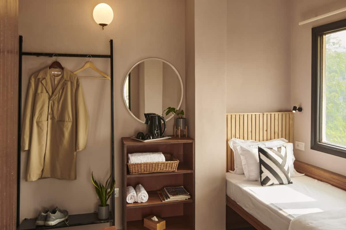 Une chambre d’hôtel moderne comprenant un lit, une chaise en bois, une table, un miroir, une étagère avec des serviettes et une fenêtre donnant sur un paysage agréable.