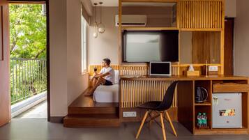 A modern room with a wooden desk, a TV, and a chair. There is a staircase leading to a balcony with a railing.