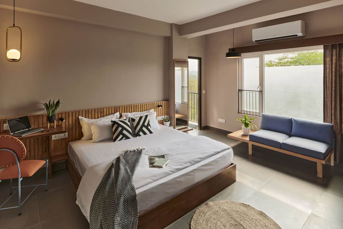 Une chambre d’hôtel moderne dotée d’un grand lit, d’un bureau avec un ordinateur portable, d’un canapé et d’un balcon offrant une vue agréable.