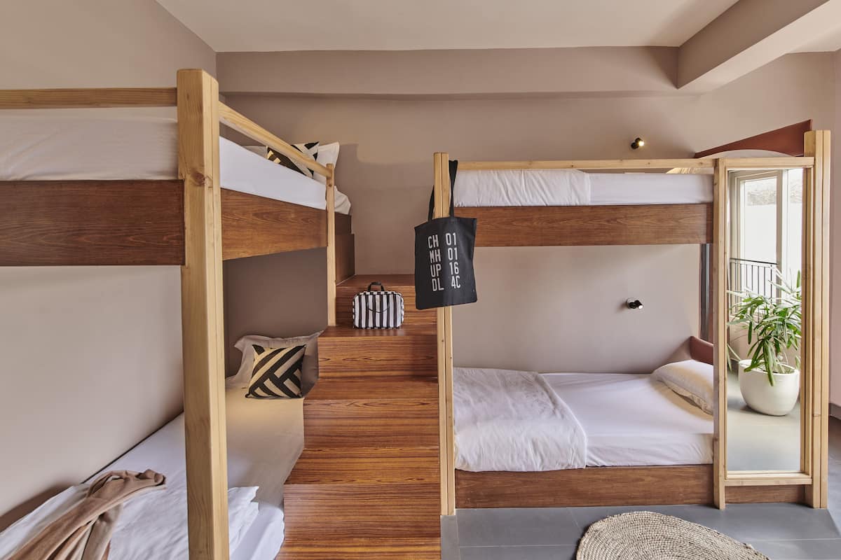 Une chambre avec un lit superposé doté d’une tête de lit en bois, un petit sac et un miroir.