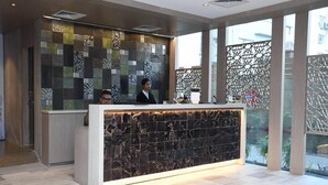 A reception desk with a patterned tile wall, a receptionist, and a modern interior design. - Lynq Aero (Barasat)
