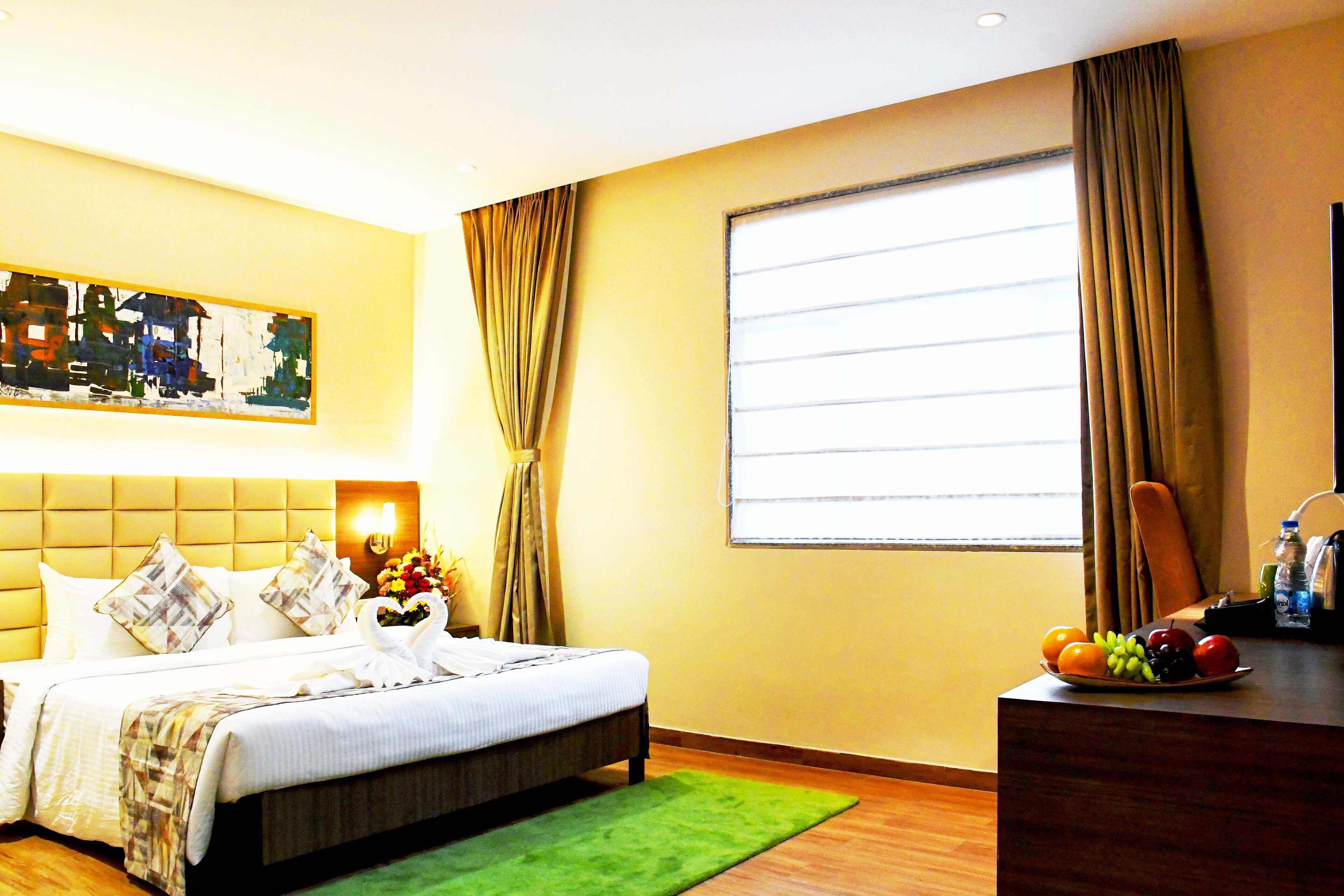 A hotel room with a bed, a green rug, a fruit bowl, and a painting on the wall.