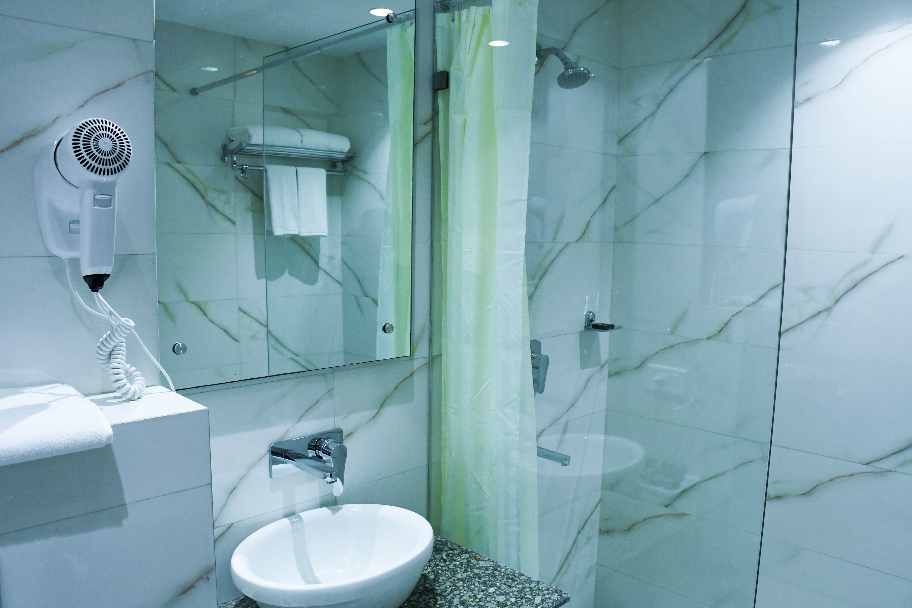 Ein modernes Badezimmer mit einer Duschkabine aus Glas, einem weißen Waschbecken und einem an der Wand montierten Fön.