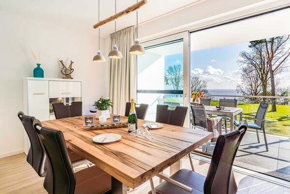 Un espace repas moderne avec une table en bois, des chaises noires et des luminaires suspendus. Une grande fenêtre offre une vue sur l’extérieur.