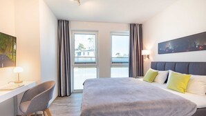 A modern hotel room with a large bed, a desk with a chair, and a cityscape view through the windows. - Apartment Wolkenschiff - Oasis on the lagoon - Wolkenschiff (6-3) (Garz/Usedom)