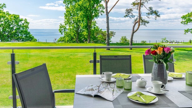 A table set for two with a view of a grassy area and trees, a vase of flowers, and a menu. - Apartment Wolkenschiff - Oasis on the lagoon - Wolkenschiff (6-3) (Garz/Usedom)