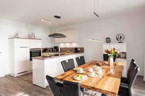Une cuisine moderne avec des meubles blancs, une table à manger en bois et des chaises noires.