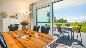 Un comedor con una mesa de madera, sillas y vista a un campo verde a través de amplios ventanales.