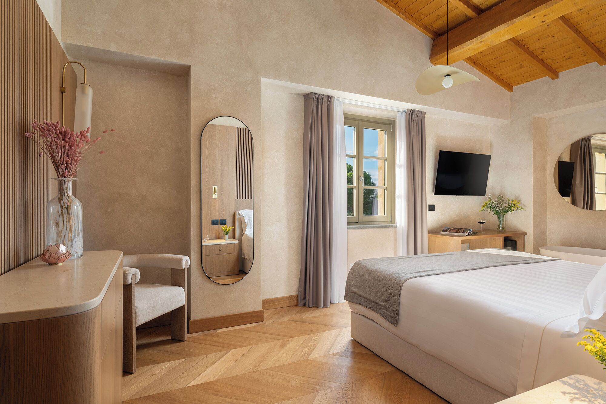 Une chambre d’hôtel avec un lit, une table de chevet, un miroir, une télévision et une fenêtre avec des rideaux.