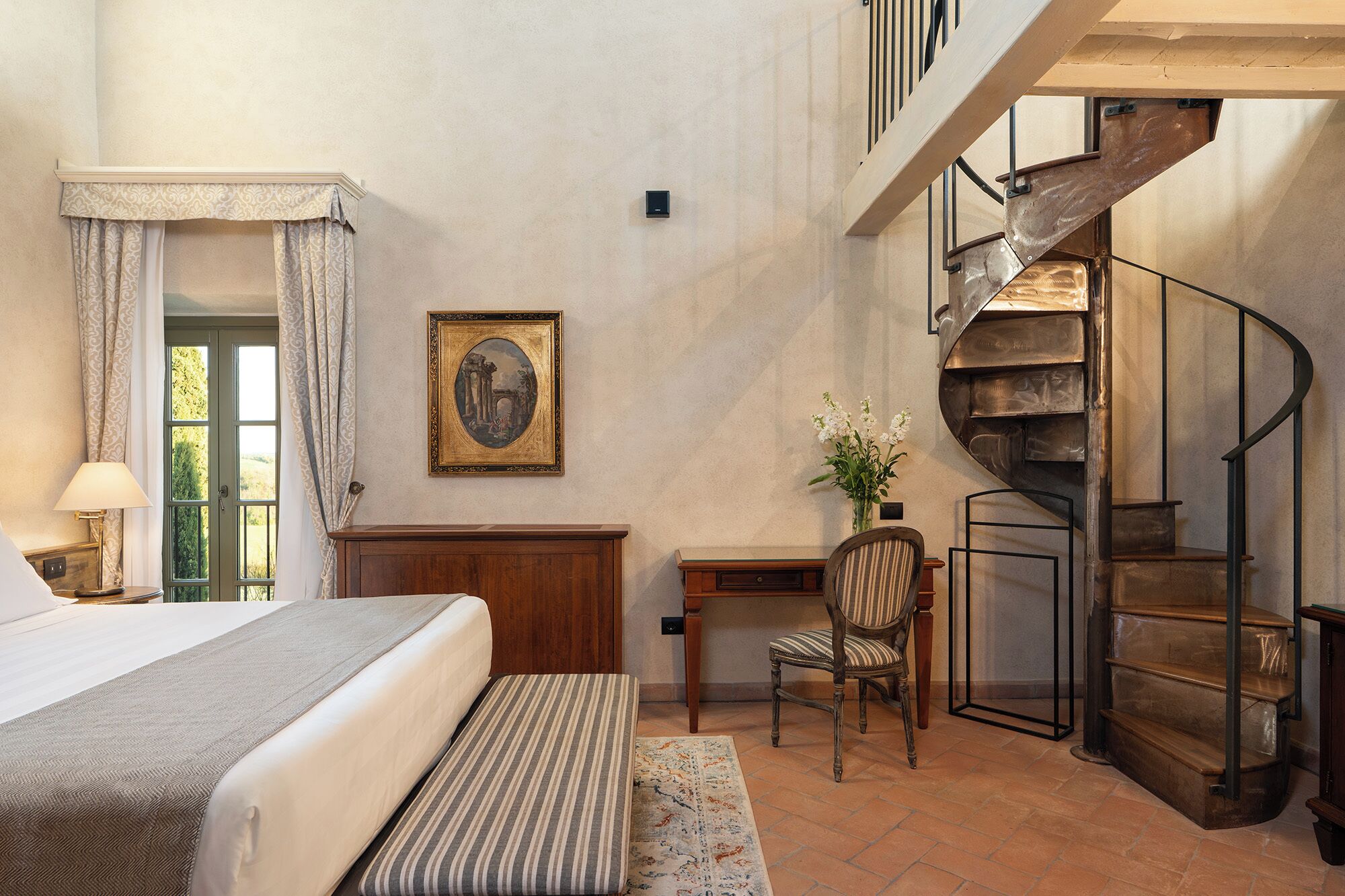 Ein Schlafzimmer mit Bett, Schreibtisch, Stuhl, einem gerahmten Bild und einer Wendeltreppe.