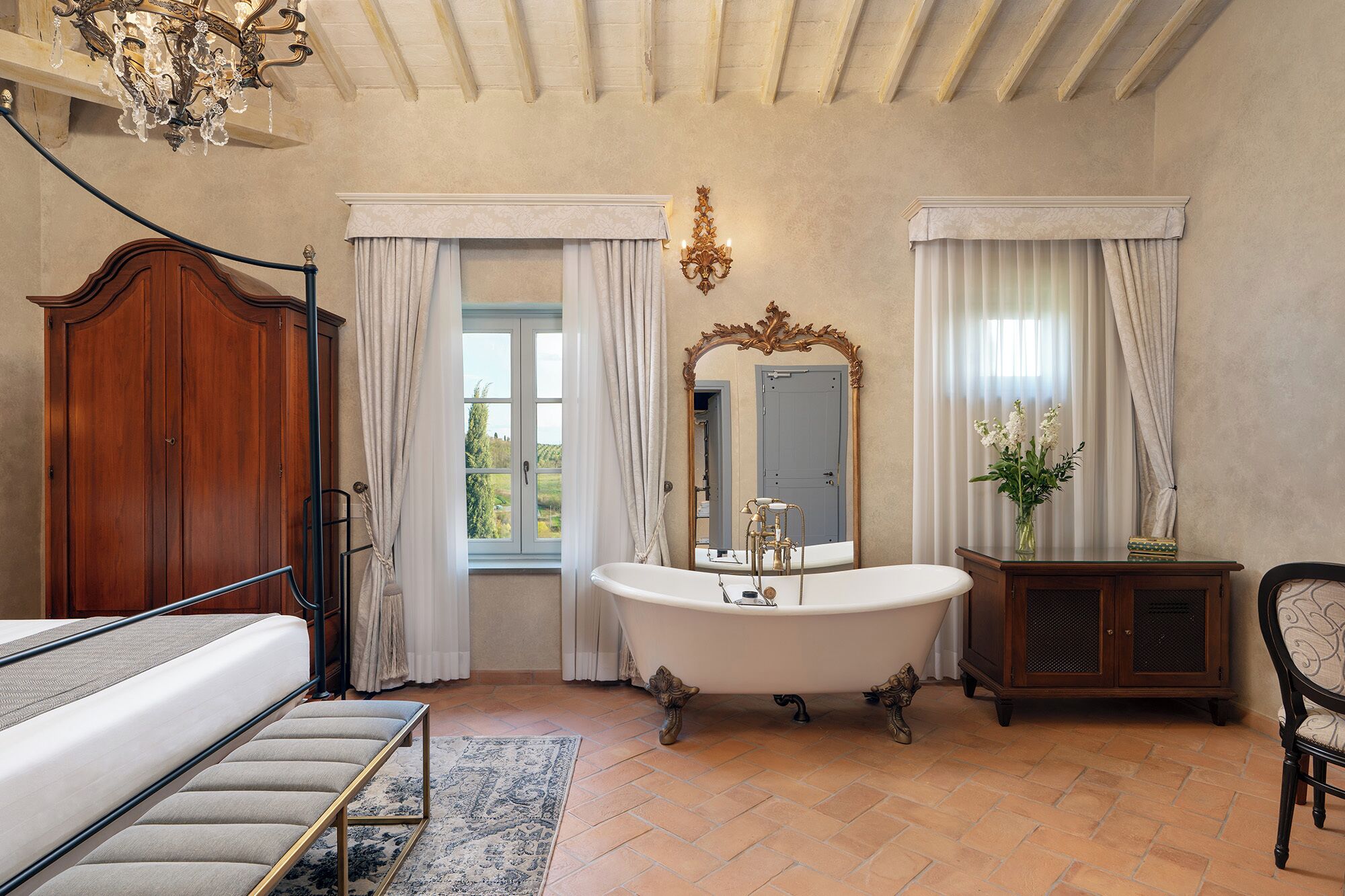 Ein Badezimmer mit freistehender Badewanne, einem hölzernen Kleiderschrank, einem Spiegel mit aufwendiger Rahmung und einer Chandelüstere.
