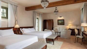 A hotel room with two beds, a wooden ceiling, chandeliers, a sofa, a chair, a cabinet, and a painting on the wall.
