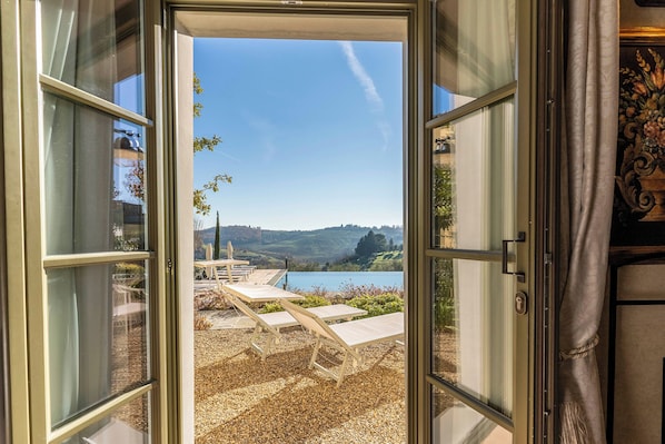 A doorway leading to a pool area with outdoor furniture and a scenic view of hills and water.
