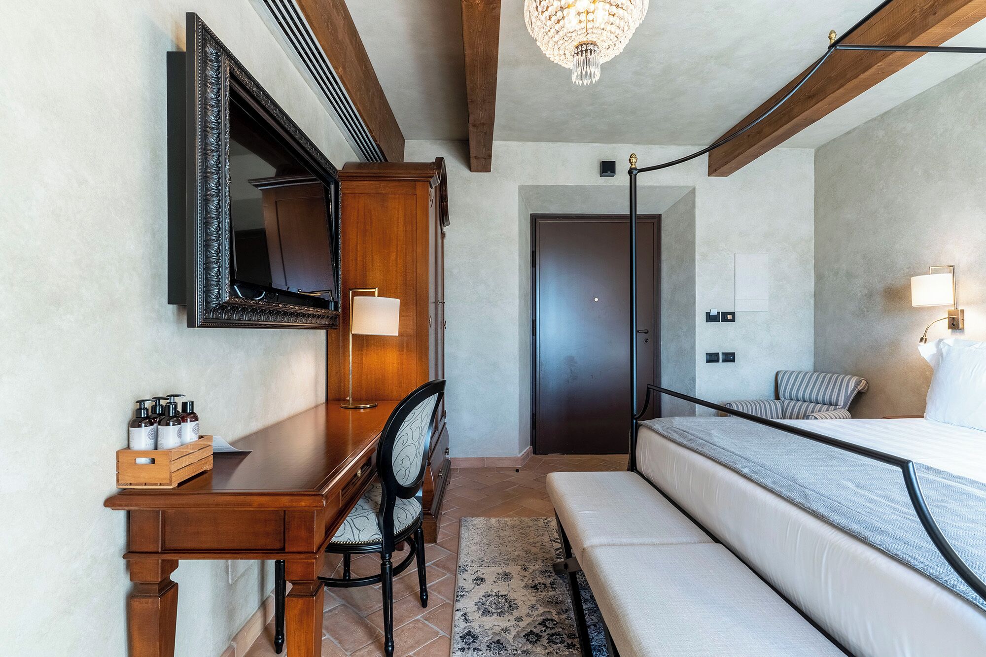 Une chambre à coucher comprenant un lit, un bureau, une chaise, un miroir, un lustre et une porte.
