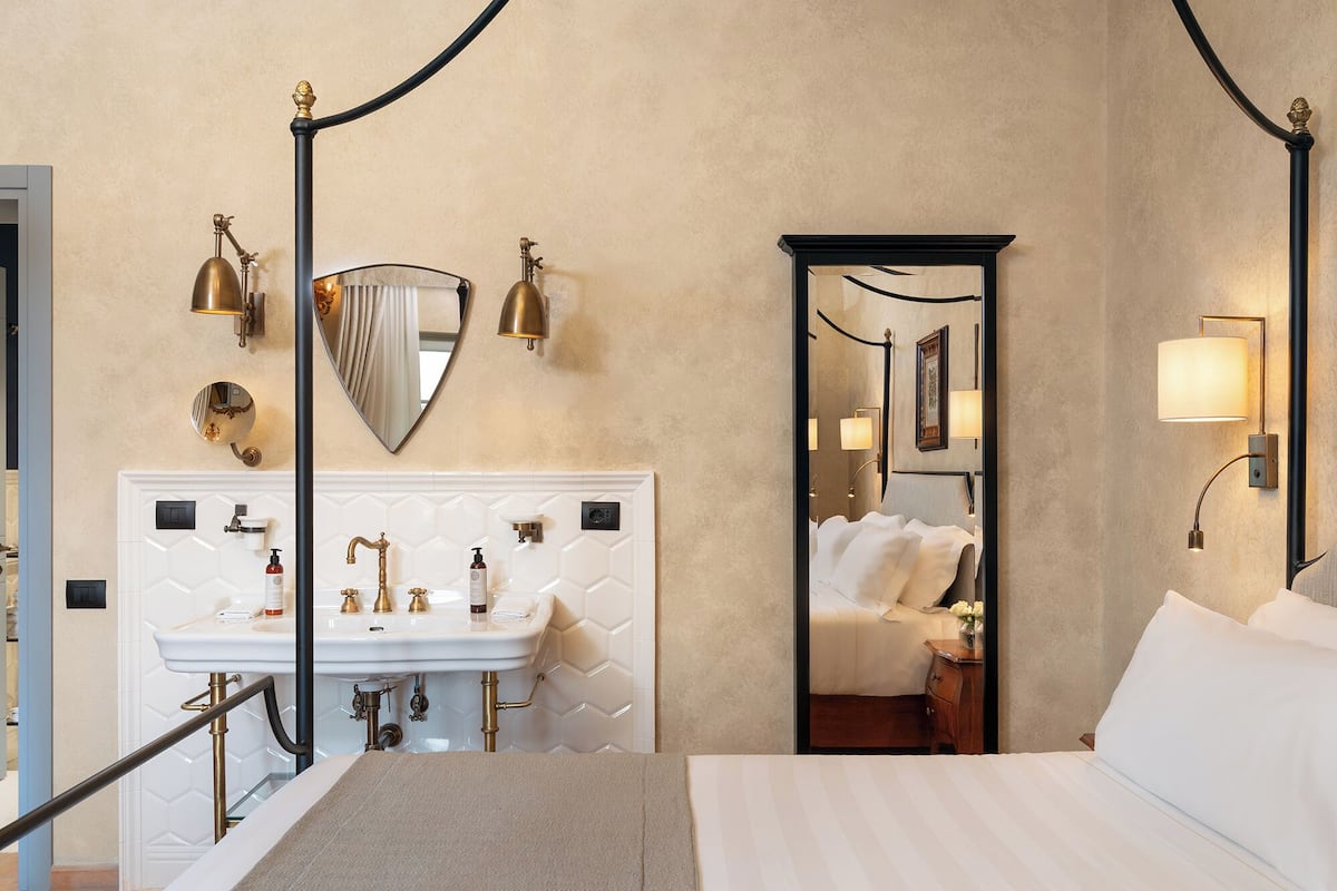 Ein Hotelzimmer mit Bett, Badezimmer mit Waschbecken und Spiegel sowie Blick in einen weiteren Raum.