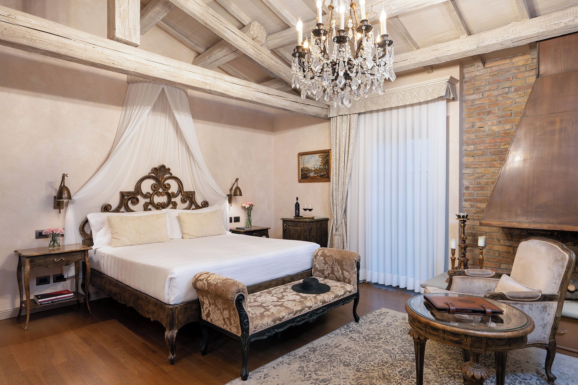 Un dormitorio con cama con dosel, candelabro, chimenea y una zona de estar con una mesa.