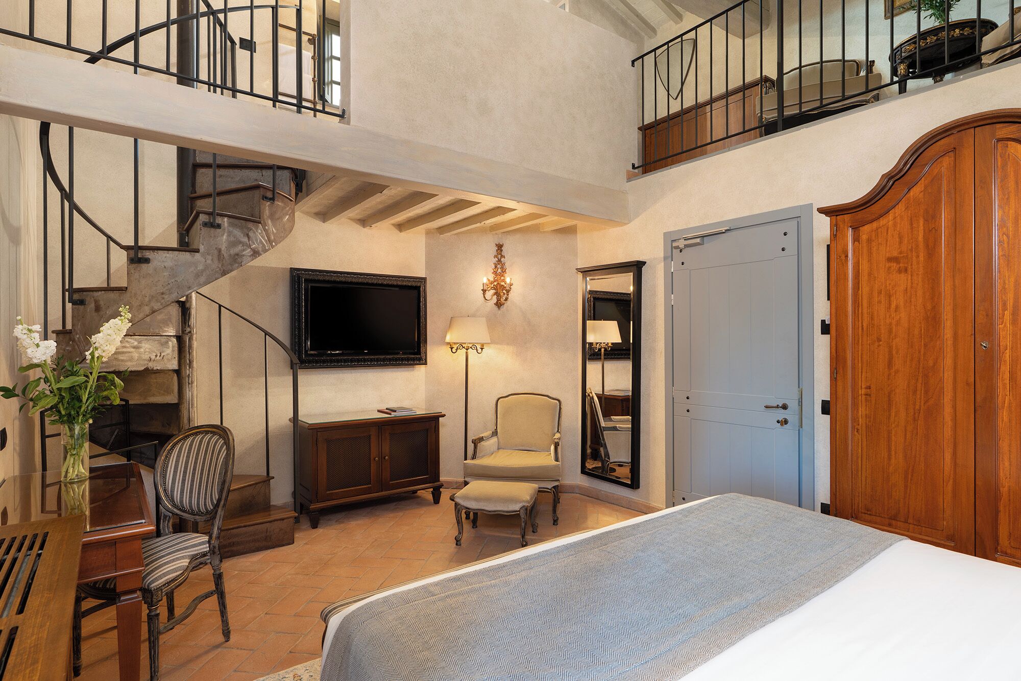 Um quarto espaçoso com uma cama grande, televisão, uma cadeira, guarda-roupa de madeira e um lance de escadas.
