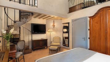 Een ruime slaapkamer met een groot bed, een televisie, een stoel, een houten garderobe en een trap.