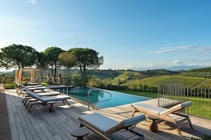 Zona junto a la piscina con sillones de descanso, una pérgola y vistas a colinas onduladas.