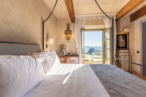 A hotel room with a large bed, a nightstand with a lamp, a mirror, and a view of the outdoors.
