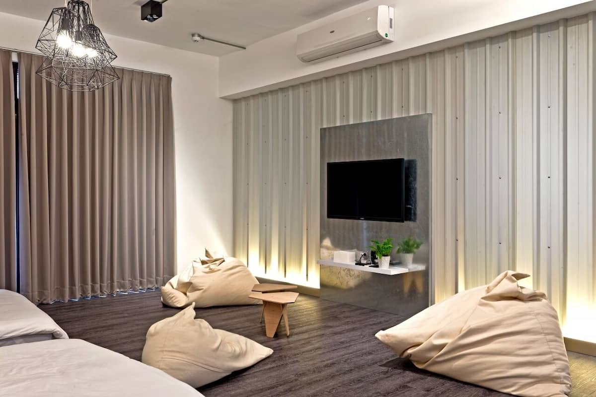 Quarto moderno com uma cama grande, televisão na parede, uma mesinha e poltronas de saco.