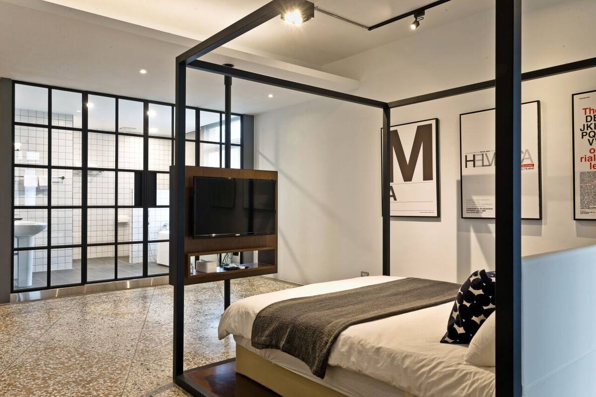 Quarto moderno com uma cama grande, televisão e vista para um banheiro através de um painel de vidro.