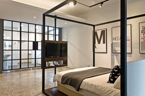 Une chambre moderne avec un grand lit, une télévision et une vue sur la salle de bain grâce à une paroi en verre.