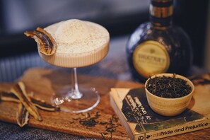 A cocktail in a glass with a decorative garnish, a bottle of liquor, a bowl of tea, and a book titled "Pride and Prejudice". - Island House (Kaohsiung)