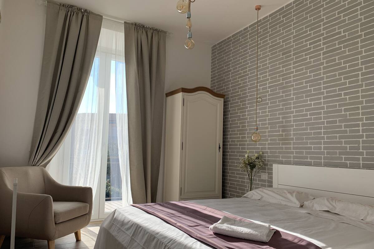 Quarto com cama, uma cadeira, guarda-roupa e parede com padrão de tijolos.