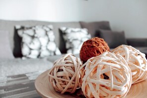 Ein Holztisch mit gewebten Kugeln und einer braunen Kugel, vor verschwommenem Hintergrund eines Zimmers mit Bett und Kissen.