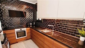 Una cocina moderna con un salpicadero de baldosas negras y marrones, armarios de madera, un horno de acero inoxidable y un fregadero.
