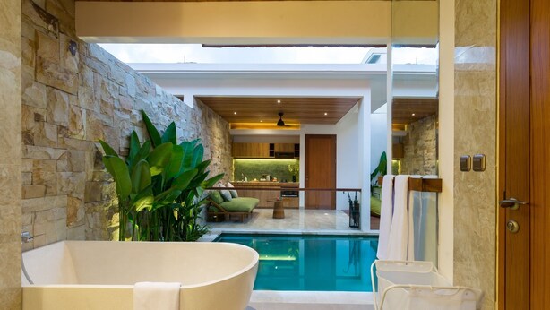 A modern bathroom with a freestanding bathtub, a glass-enclosed pool, and a stone wall. - Danka Villa (Denpasar)