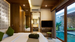 A hotel room with a large bed, a TV, a desk, and a view of an indoor pool. - Danka Villa (Denpasar)
