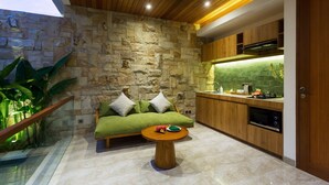 A modern kitchen with a stone wall, wooden cabinets, and a green sofa. - Danka Villa (Denpasar)