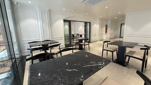A modern dining area with marble tables and chairs, recessed lighting, and a view through a glass wall.
