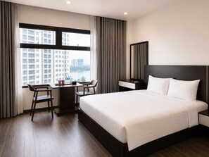 A hotel room with a large bed, a desk with two chairs, a view of buildings through the window, and a mirror on the wall. - The Nova Hotel & Apartment (Hai Phong)