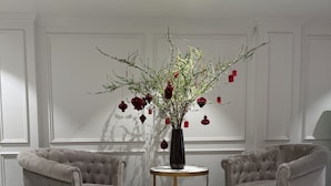 A room with two armchairs, a small round table, and a vase with branches and red ornaments.