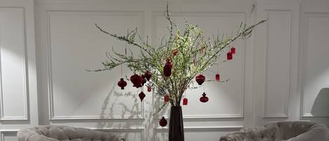 Una habitación con dos sillones, una mesita redonda y un florero con ramas y adornos rojos.